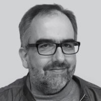 Black and white portrait of Udo Meisen, a smiling older man with dark rimmed glasses, a mustache and a beard.