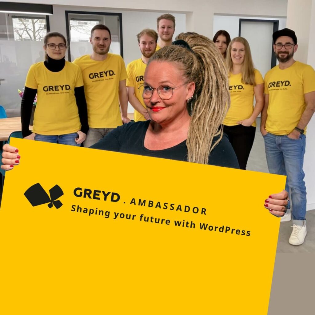 Four men and three women in the background, all wearing yellow t-shirts with the Greyd logo. In the foreground is Anne, a woman with a big blonde ponytail, holding up a yellow shield that depicts the Greyd Product Ambassador Badge.